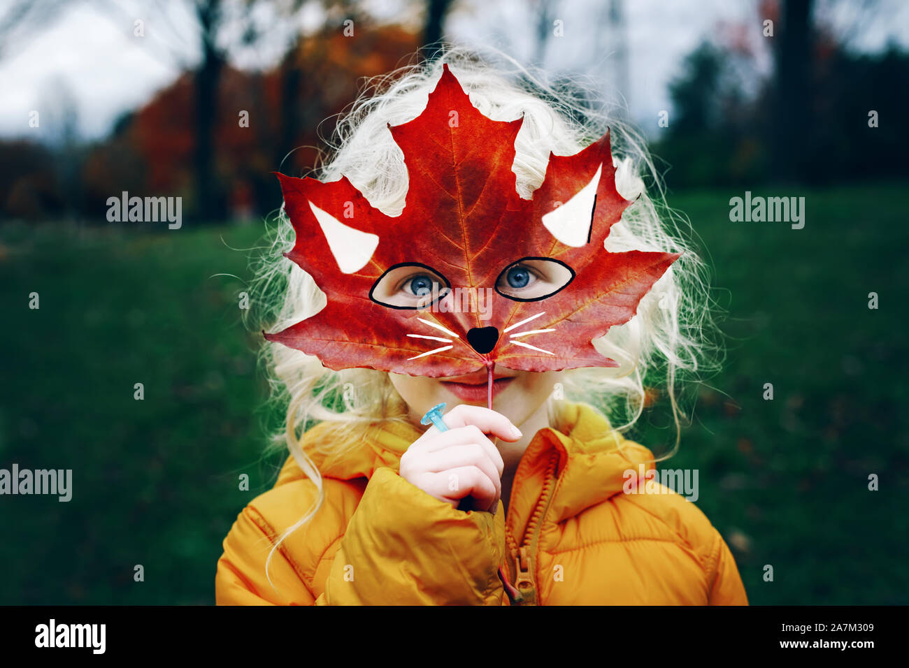 Portrait von niedlichen Kind mit blauen Augen holding Herbst Red maple leaf Bemalte Maske vor dem Gesicht. Mädchen spielen vorgibt, Fox Katze sein. Fee Stockfoto