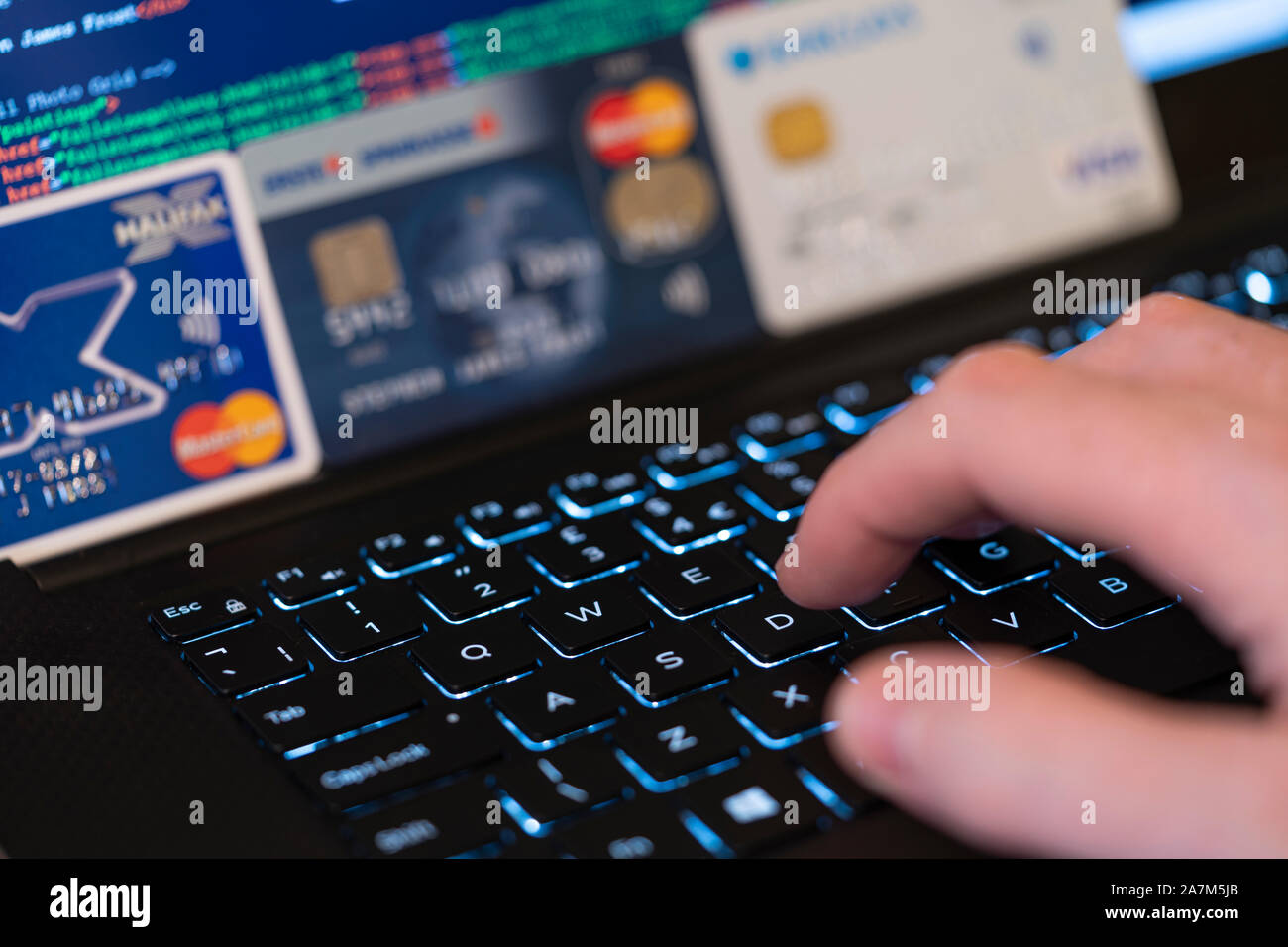 Eine Hand, die Eingabe über eine Tastatur mit Bildschirm und Kreditkarten im Hintergrund. Konzept: Betrug mit gestohlenen Kreditkarten online Zahlung zu machen Stockfoto