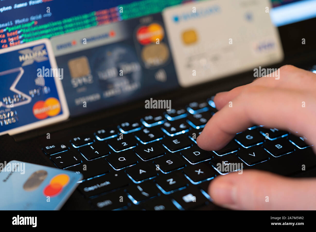 Eine Hand, die Eingabe über eine Tastatur mit Bildschirm und Kreditkarten im Hintergrund. Konzept: Betrug mit gestohlenen Kreditkarten online Zahlung zu machen Stockfoto
