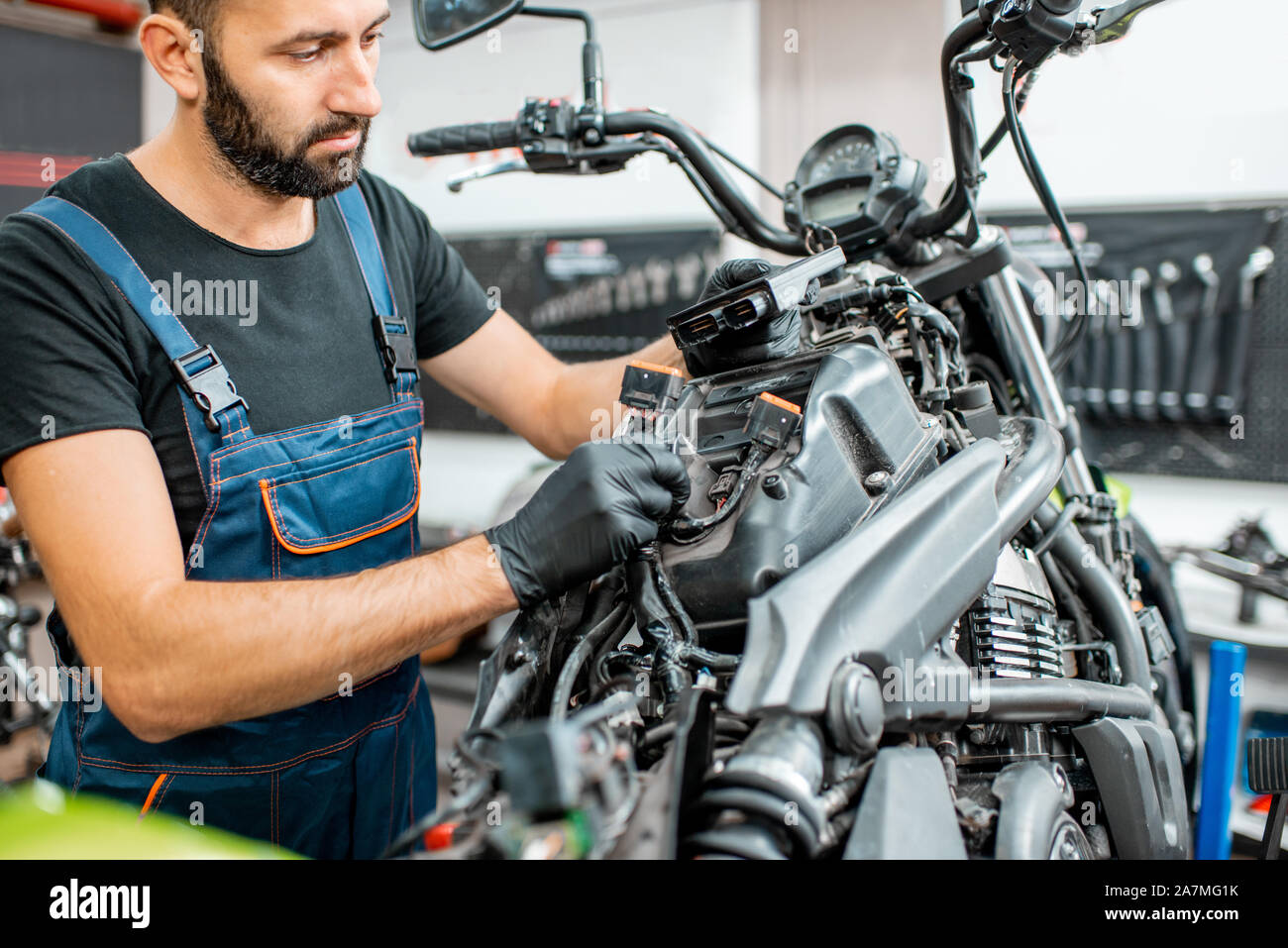 Elektriker oder Schlosser in Schutzhandschuhe verbinden Verkabelung im Motorrad während einer Reparatur in der Werkstatt Stockfoto