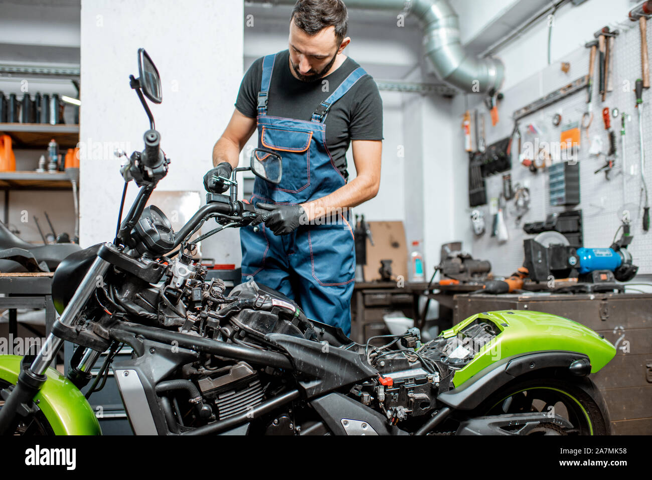 Mechaniker in Latzhosen Motorrad reparieren, Messen spiegel halter für  Ersatz oder Tuning bei dem Workshop im Innenbereich Stockfotografie - Alamy