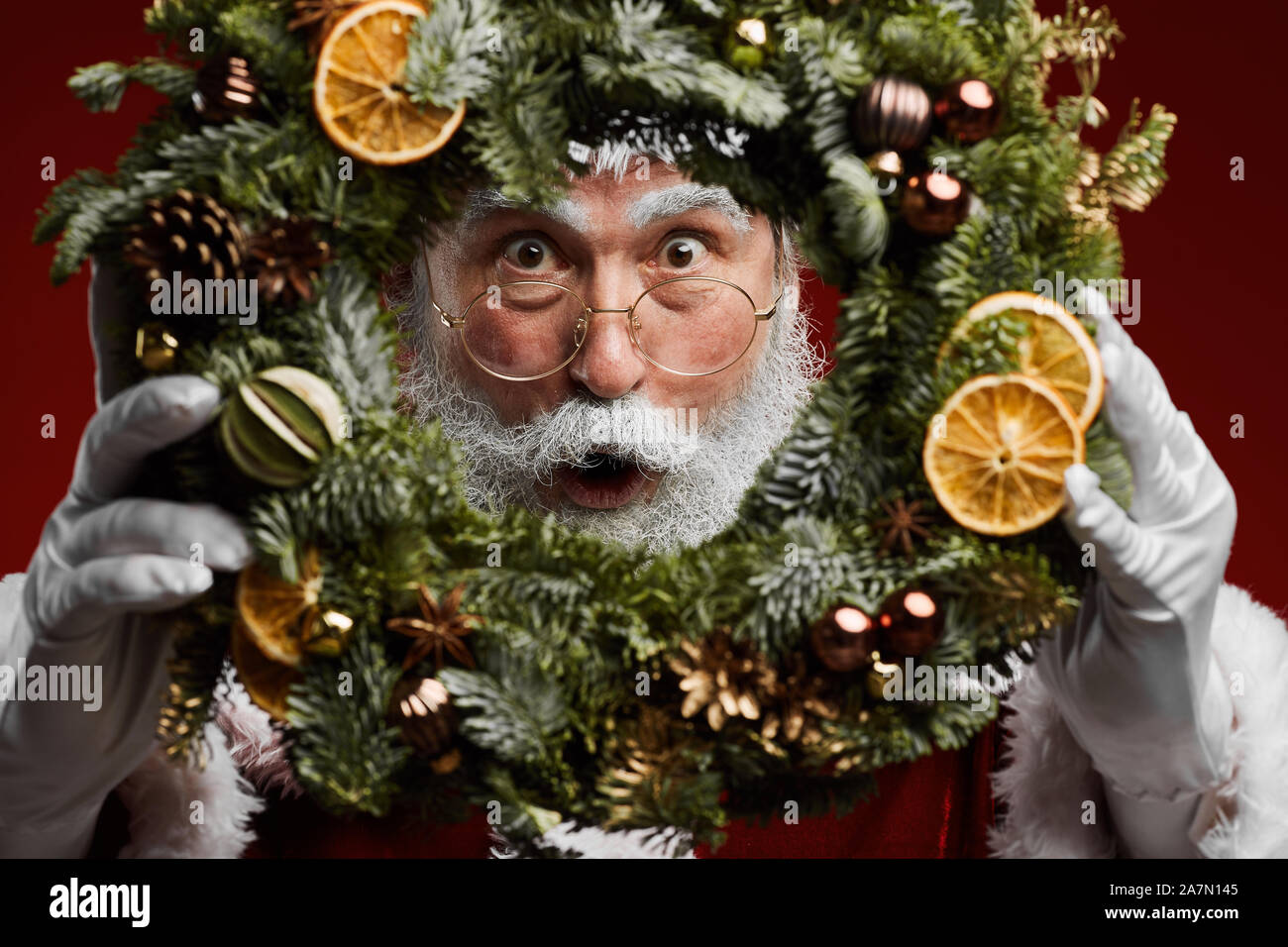 Closeup Portrait von classic Santa Claus Christmas Mädchen mit Kranz und spähen an Kamera Stockfoto