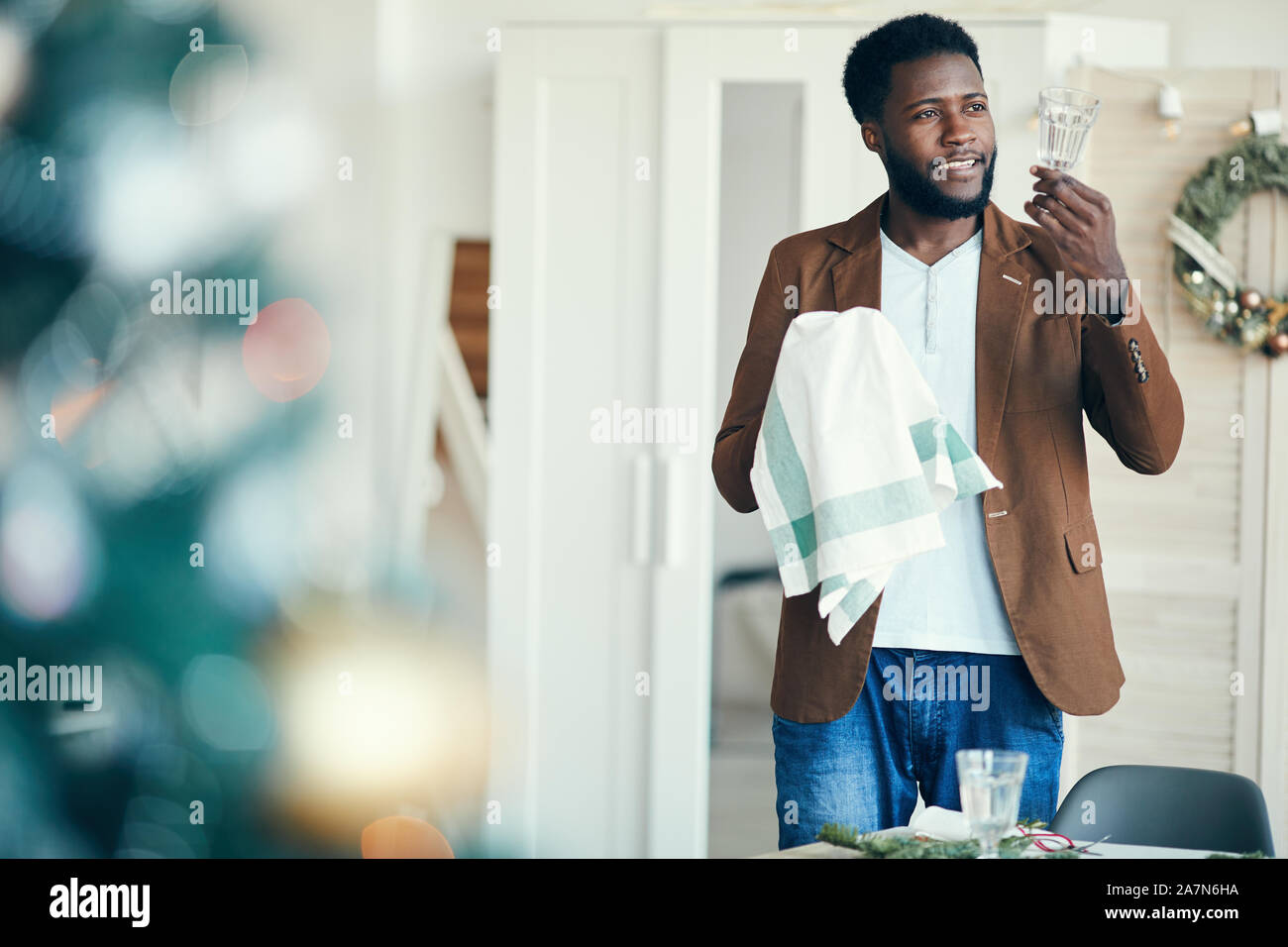 Taille bis Portrait von lächelnden Afrikaner Mann wischen Kristallgläsern beim Einstellen der Tisch für Weihnachtsfeier, kopieren Raum Stockfoto