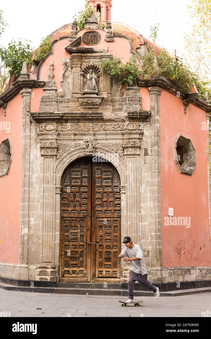 Ein Junge auf einem Skateboard übergibt die kleine barocke Kapelle von La Concepción Cuepopan auch als La Conchita oder die Kapelle der Toten in der Concepcion Platz von Mexiko-Stadt, Mexiko kennen. Stockfoto