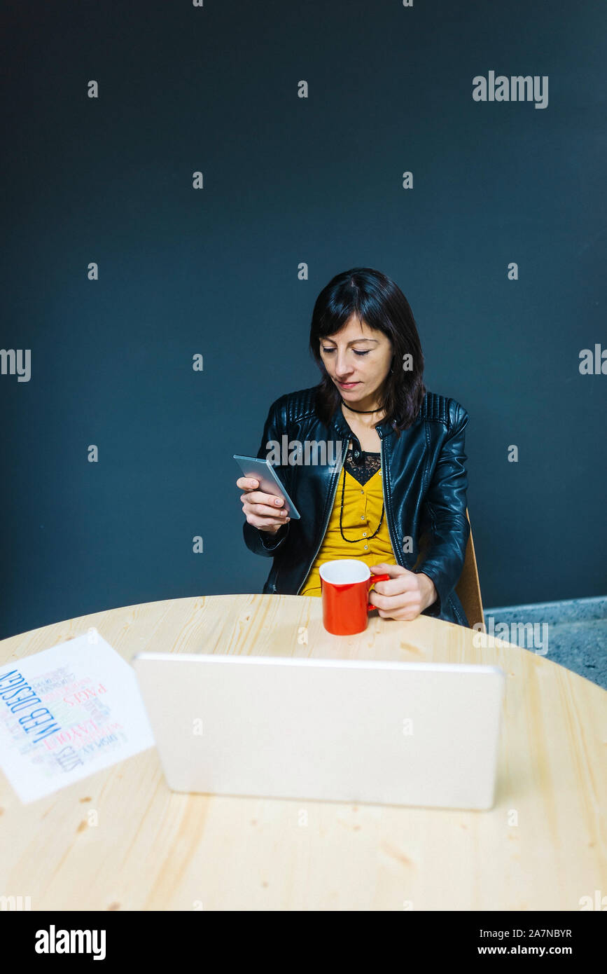 Frau mit Kaffee und Smartphone in Ihrem Büro Stockfoto