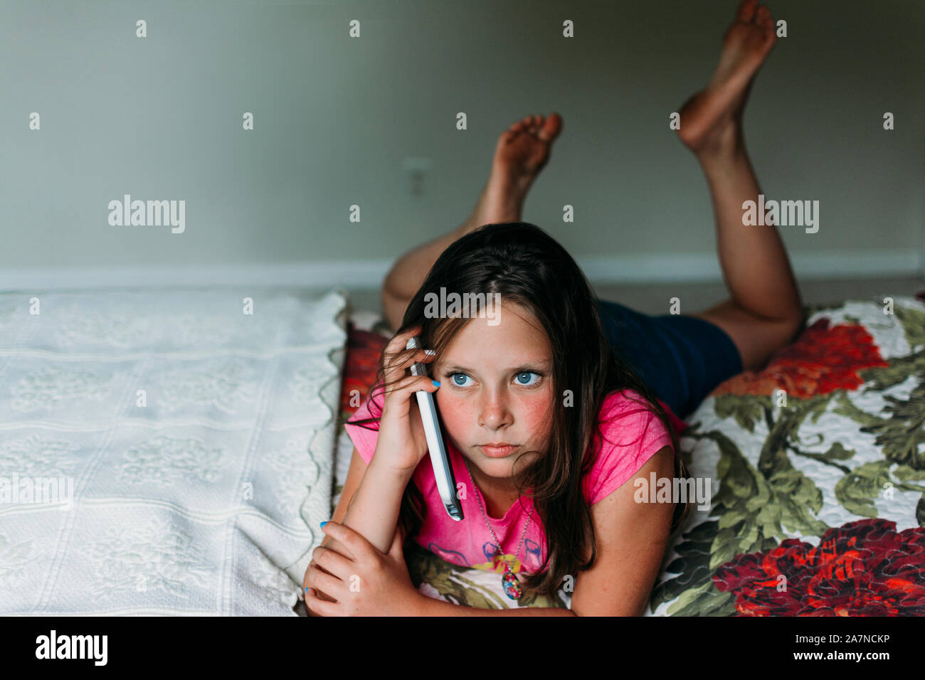 Tween Girl Festlegung auf ein Bett mit einem Mobiltelefon Stockfoto
