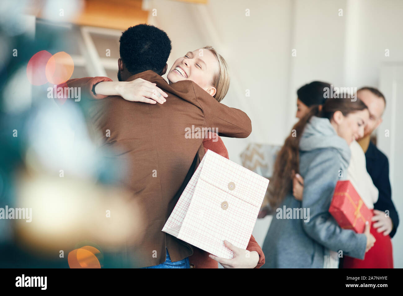 Gruppe der modernen jungen Menschen den Austausch von Geschenken während der Weihnachtsfeier, Fokus auf lächelnde Frau umarmen Freund im Vordergrund, Kopie Raum Stockfoto