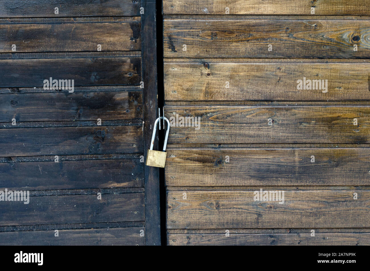 Nahaufnahme der ein geschlossenes Vorhängeschloss auf einer lackierten braunen Kiefer Holz- Hintertür. Stockfoto