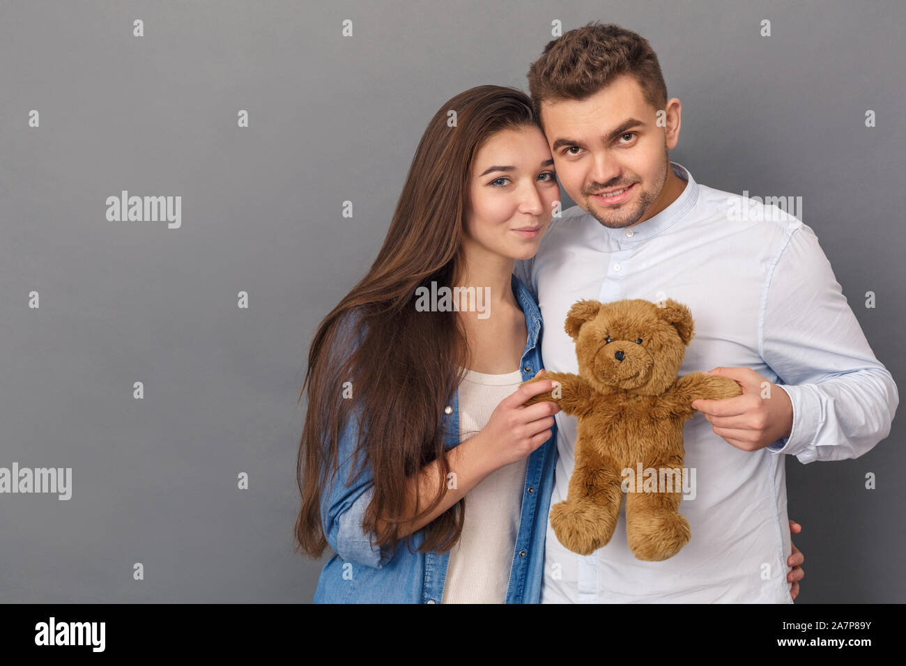 Beziehung Konzept. Junges Paar Studio stehen isoliert auf Grau mit Teddybär posiert für die Kamera cute Stockfoto