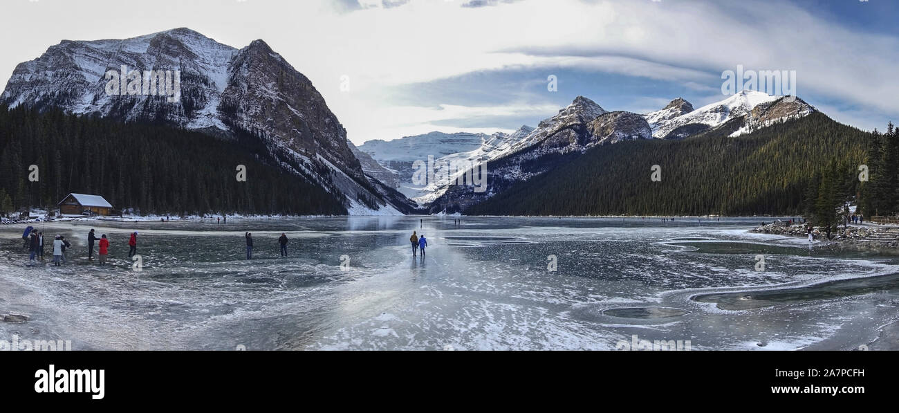 Touristen Menschen Wandern und Schlittschuhlauf Lake Louise Frozen Surface Ice. Panoramalandschaft Entfernte Kanadische Rocky Mountain Peaks Winter Skyline Stockfoto