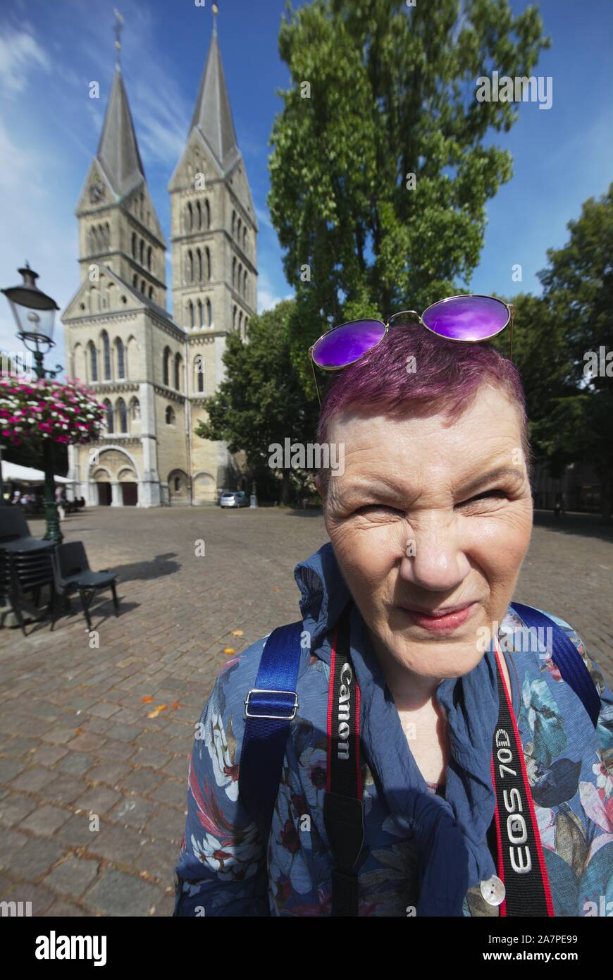 Portrait von Frau Sommer Tourist mit geschlitzten Augen und verzerrte Gesicht von Ultra Wide Angle Shot mit mittelalterlichen Kirche und grüne Bäume im Hintergrund Stockfoto