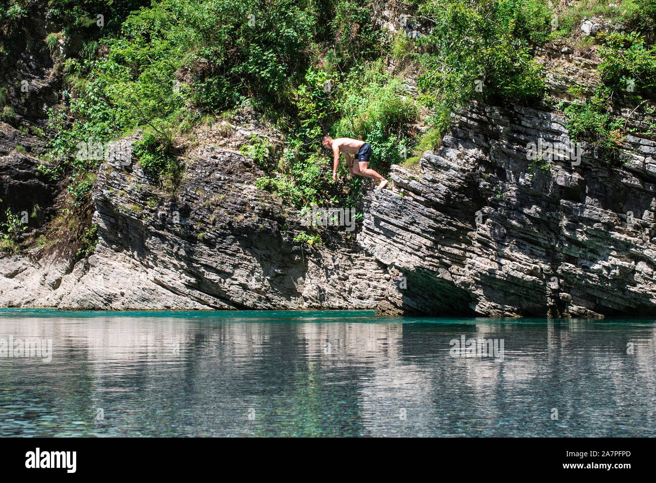 Ein Mann springt von einer Klippe in einem Fluss. Sommer, Spaß, Mann springt wie Fische im See, schwimmt, genießt die Zeit auf die Sommerferien. Stockfoto