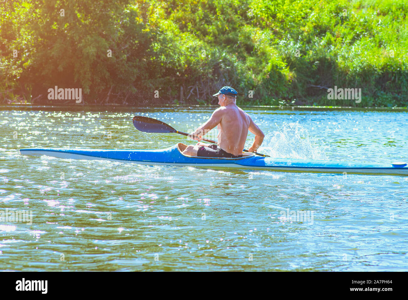 Man paddeln eine blaue und gelbe Kajak auf dem Fluss in der Nähe der Küste. Kajak Konzept. ein Mann schwimmt in einem Kanu auf dem Fluss. Ein Mann in einem Boot auf einem sonnigen Stockfoto