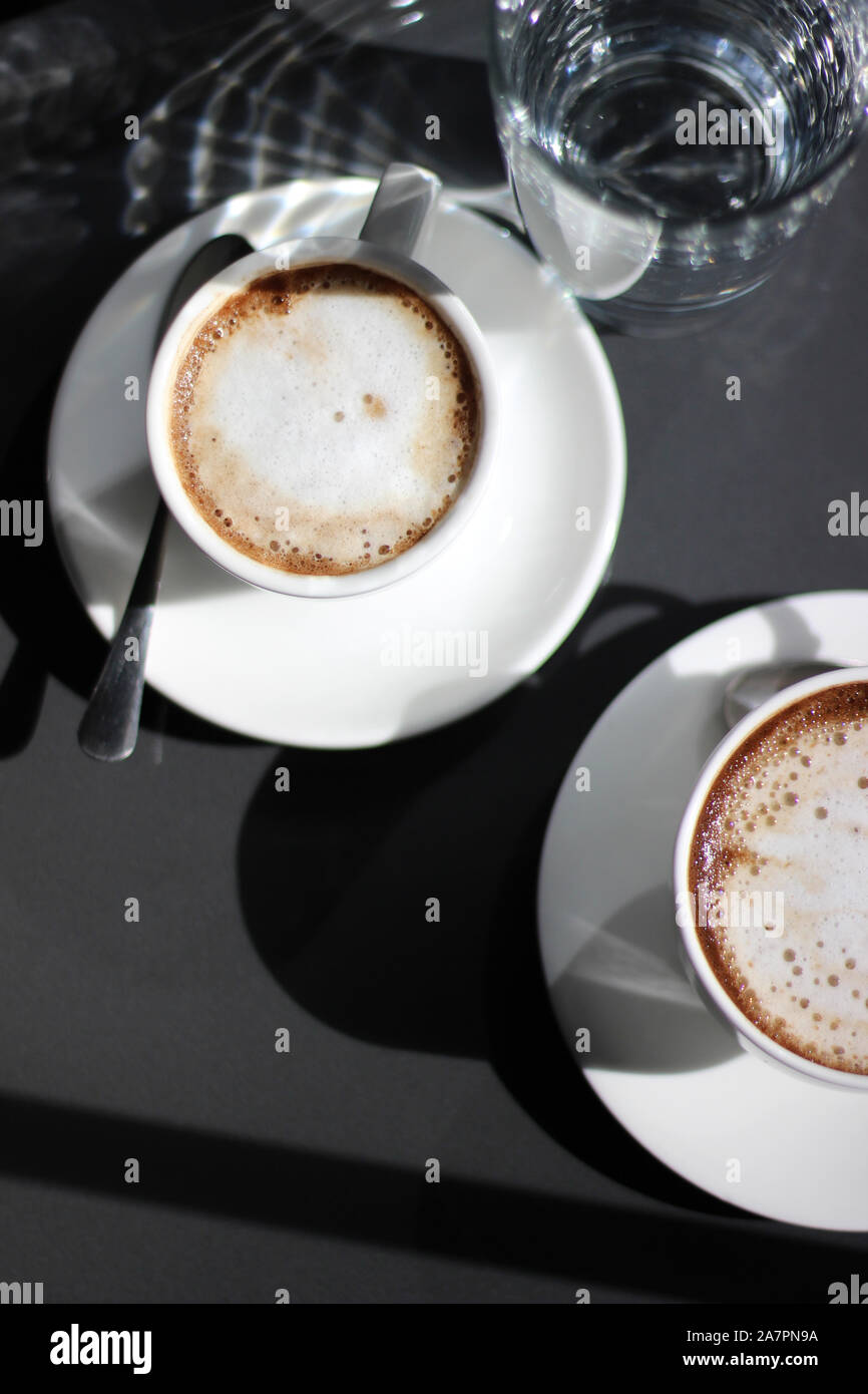 Frisch Gebrühter Cappuccino in Demitasse Cups mit Glas Wasser. Kaffee Trinken. Stockfoto