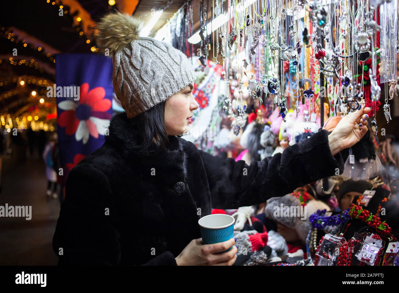 Glückliche junge Frau Wahl Weihnachten Dekoration am Markt. Modell tragen stilvolle Pelzmantel, gestrickte Mütze Hut. Outdoor Foto Stockfoto