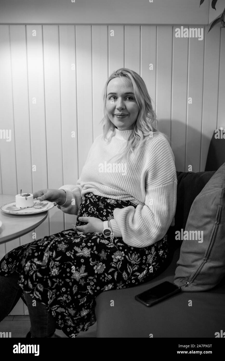 Portrait von schöne schwangere Frau Kuchen essen im Restaurant. Sie hält ihren Bauch mit einer Hand. Stockfoto