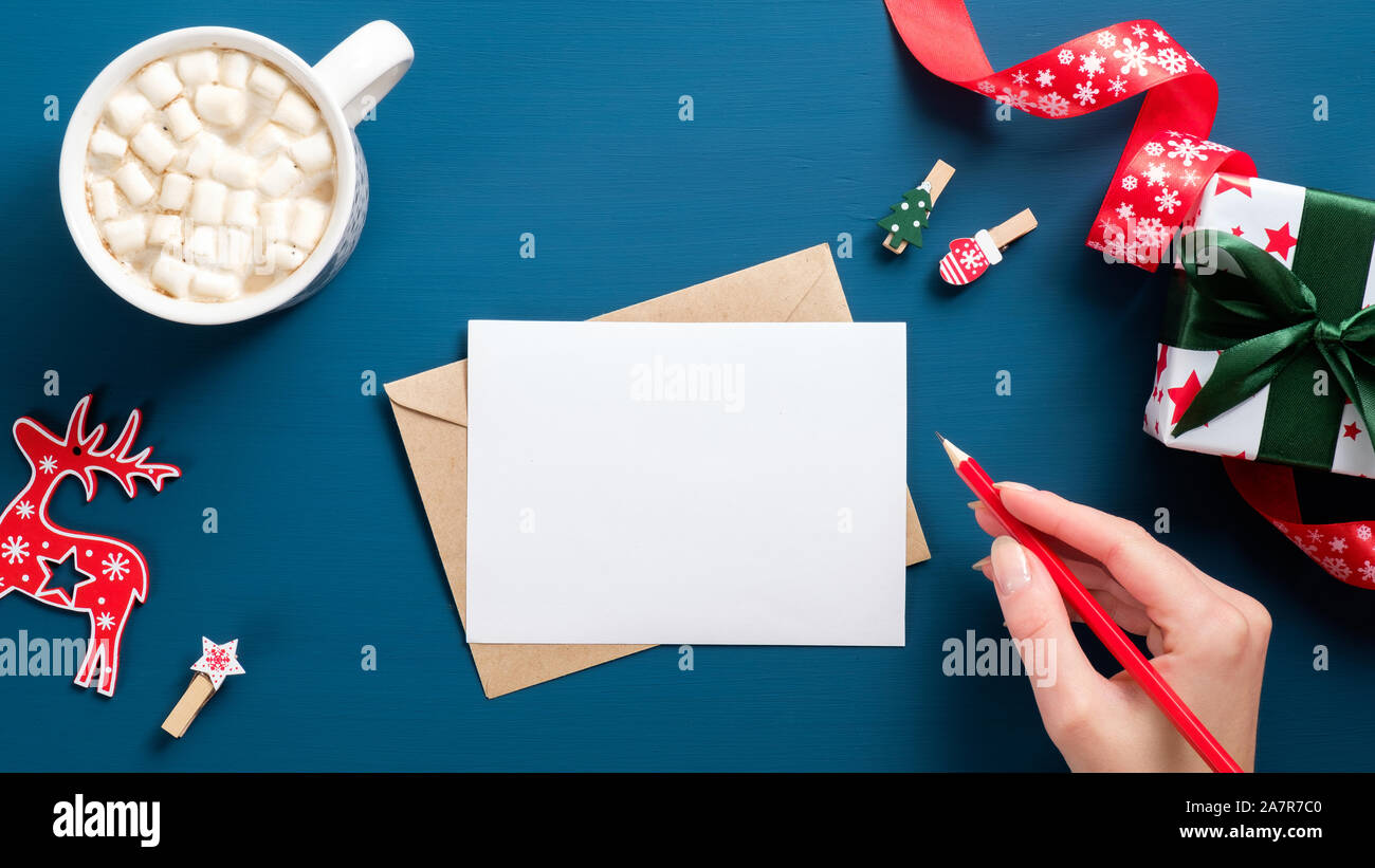 Weibliche Hand schreiben Brief an Santa Claus auf dunkelblauem Hintergrund mit Geschenke, Dekorationen und Kaffee Tasse. Draufsicht auf vintage Tabelle. Weihnachten lette Stockfoto