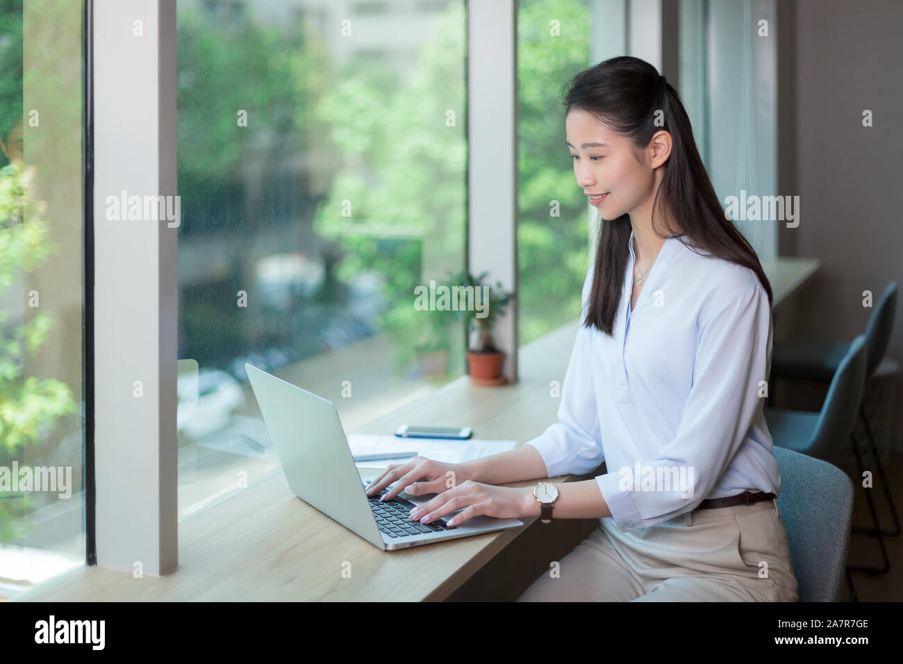 Seitenansicht Taille bis Schoß der jungen Geschäftsfrau mit geraden lange schwarze Haare mit einem Laptop an einem Schreibtisch in einem Büro Stockfoto