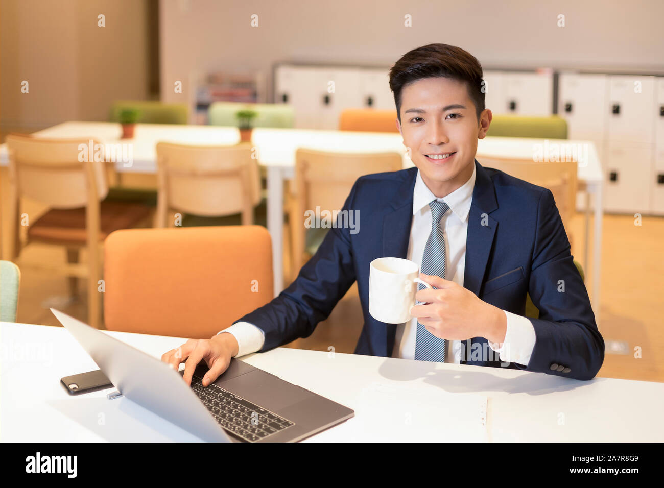 Taille bis Schuß eines junge Unternehmer mit schwarzem Haar und passen in die Kamera schaut, während Kaffee Holding Stockfoto