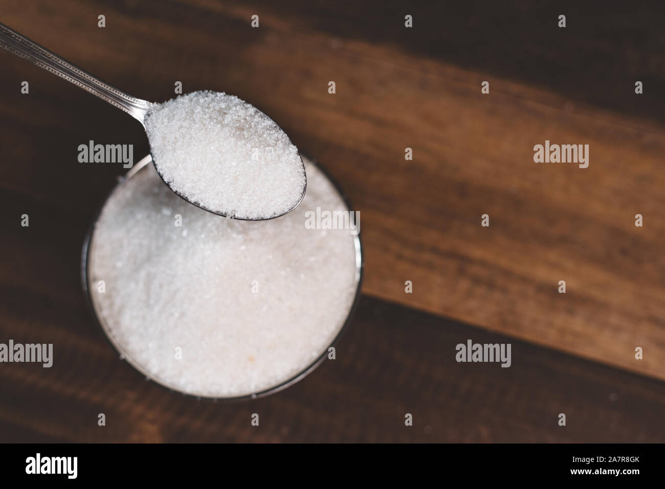 Zucker gegossen in eine Schale, auf einem Holztisch. Konzept der ungesunden Ernährung und Diabetes Stockfoto