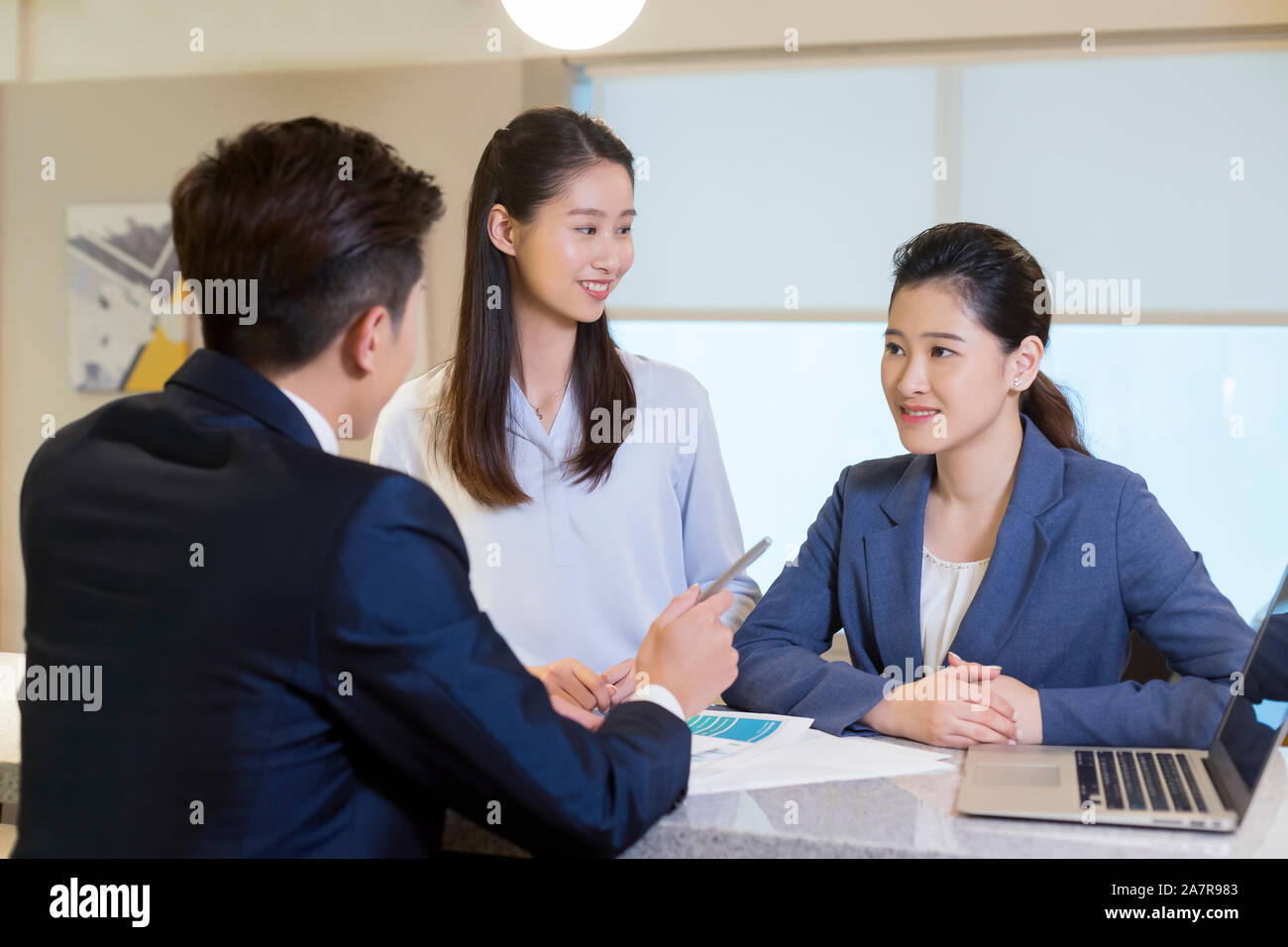 Foto von drei männliche und weibliche junge lächelnde Geschäftsleute zusammen gesprochen in einem Büro Stockfoto