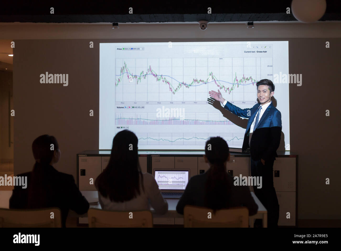 Foto von einem jungen Geschäftsmann im Anzug eine Präsentation mit einem Diagramm auf der Leinwand hinter ihm Stockfoto