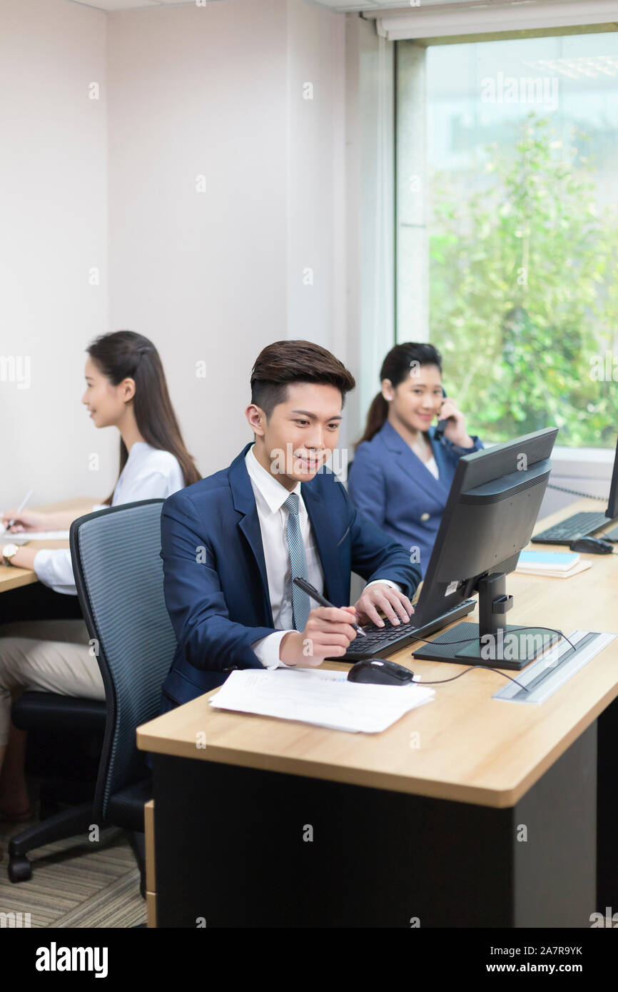 Foto: Drei junge männliche und weibliche Unternehmer arbeiten in einem Büro mit einer mit Computer und ein zweites mit Telefon Stockfoto