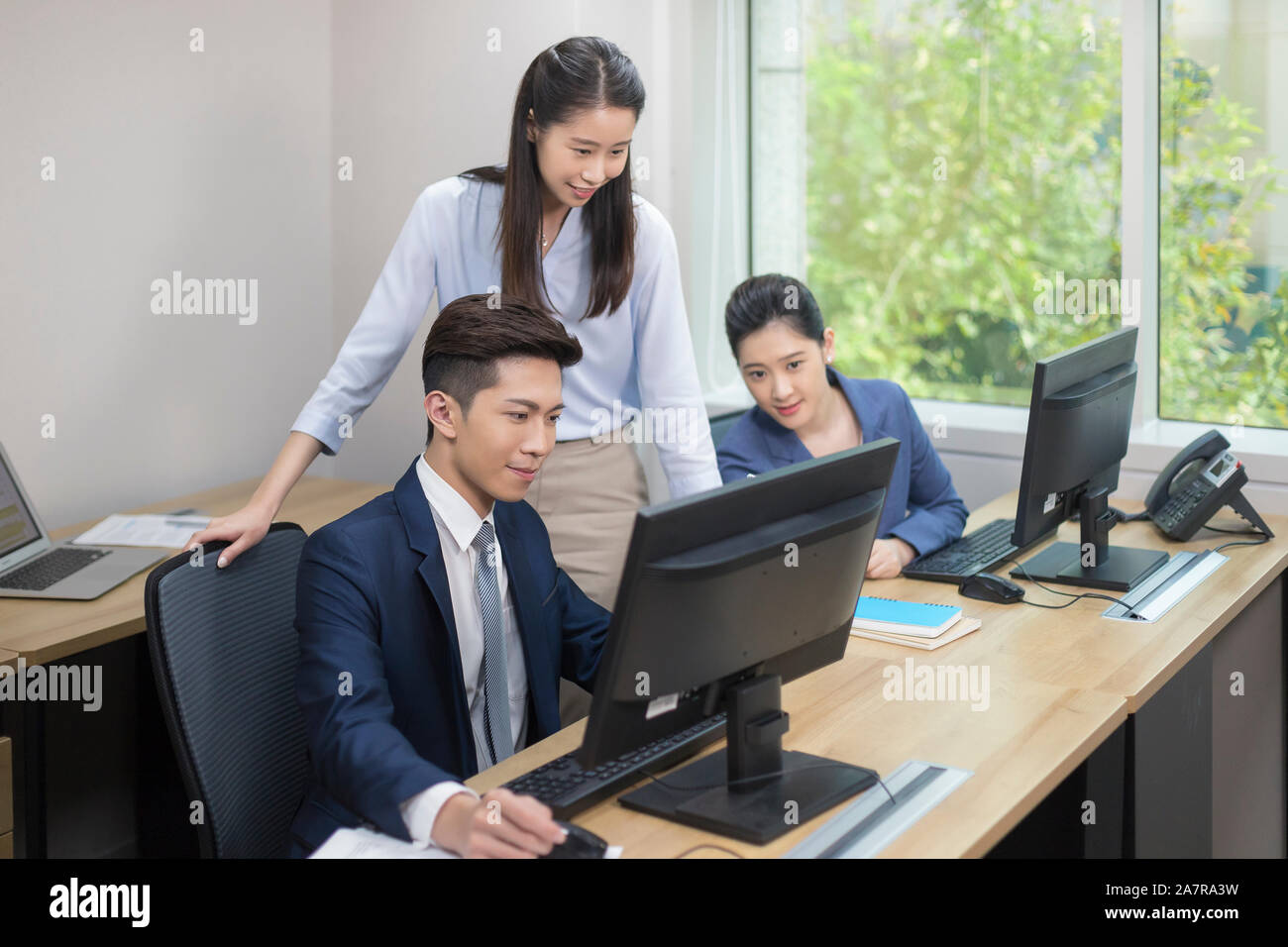 Drei lächelnden jungen männlichen und weiblichen Unternehmer auf der Suche nach einem Monitor von einem von Ihnen gleichzeitig einen Schreibtisch in einem Büro arbeiten Stockfoto