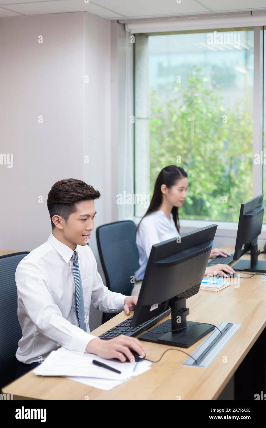 Foto von zwei jungen männlichen und weiblichen Geschäftsleuten mit ihren Computern an einem Schreibtisch in einem Büro Stockfoto
