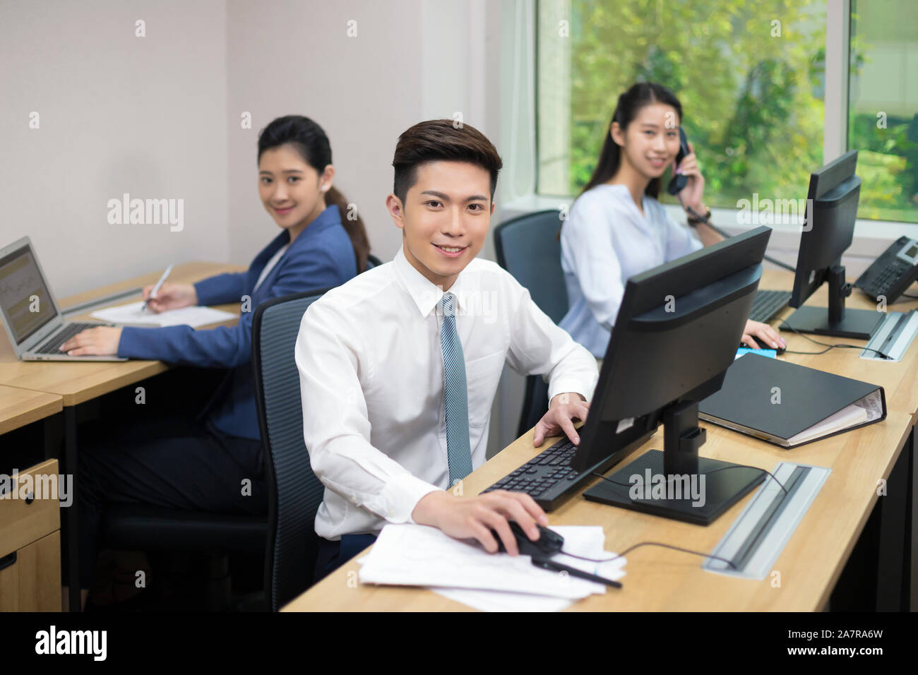 Portrait von drei junge lächelnde männlichen und weiblichen Unternehmer mit Blick auf die Kamera, während das Sitzen an Ihrem Schreibtisch in einem Büro Stockfoto