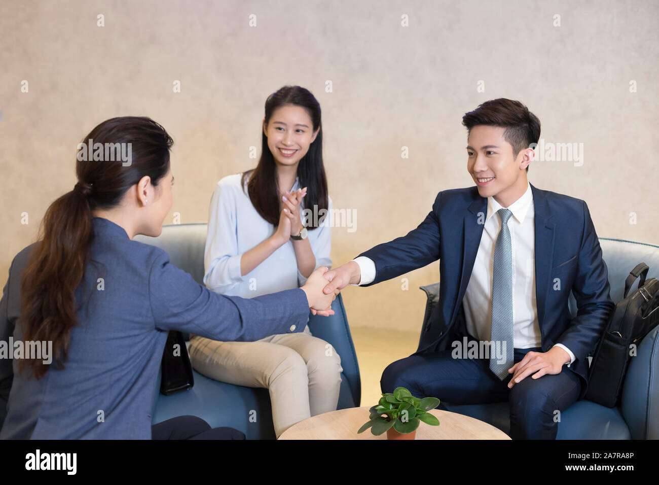 Foto von zwei junge männliche und weibliche Unternehmer die Hände schütteln bei einem Treffen mit einem anderen Klatschen und lächelnd Stockfoto