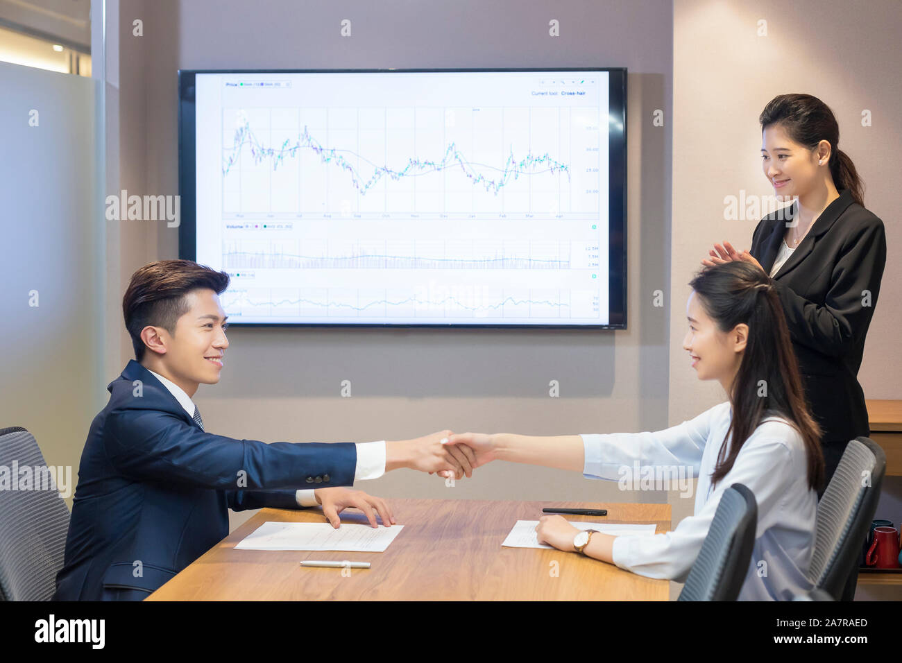 Zwei lächelnde junge männliche und weibliche Unternehmer die Hände schütteln in einem Board Zimmer bei einem Treffen mit einem anderen Geschäftsfrau klatschen Stockfoto