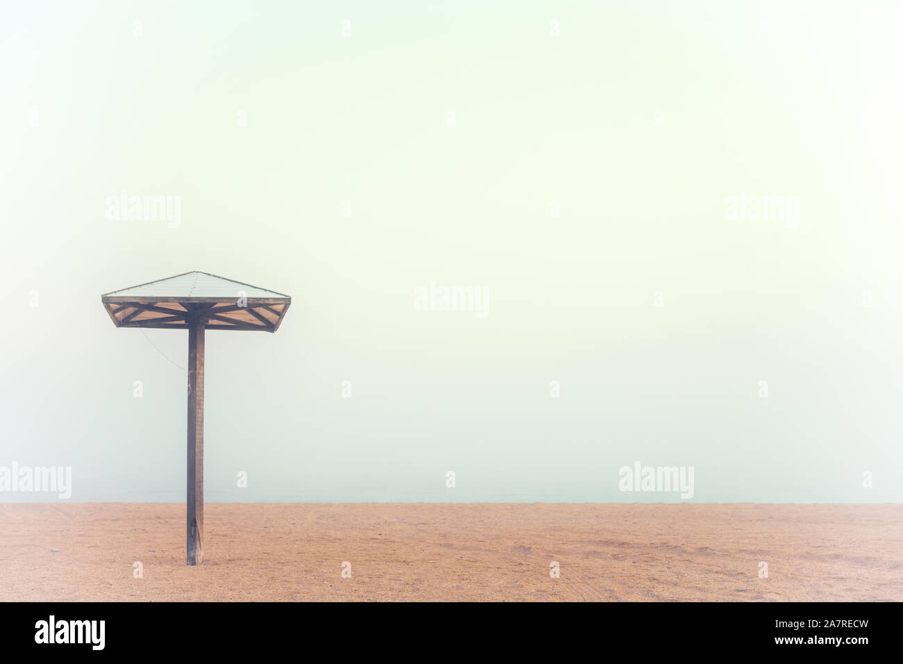 Eine Holz- Sonnenschirm auf einer leeren Sandstrand, außerhalb der Saison. Das Ende der Saison. Der Strand ist leer ohne Menschen. Stockfoto