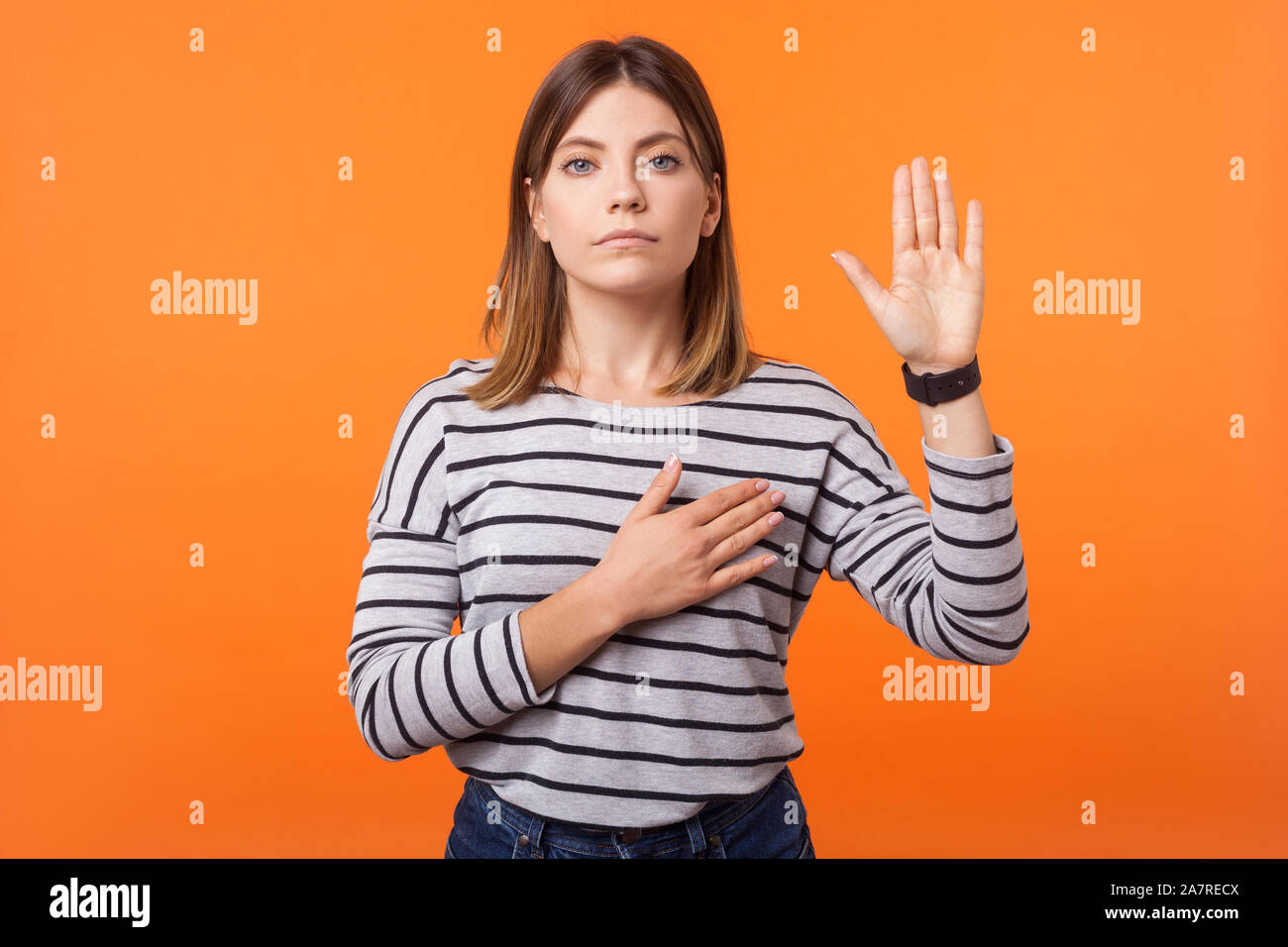 Portrait von Gläubigen, die schöne junge Frau mit braunen Haaren in Long Sleeve Striped Shirt stehend, die versprechen, mit der Hand auf der Brust und mit der Handfläche nach oben, Eid. Stockfoto