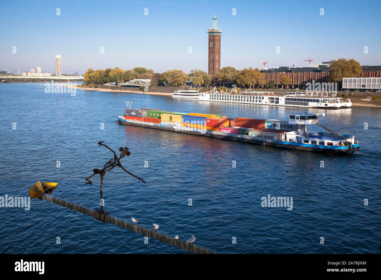 Skulptur Brueckenmaennchen auf einer Halterung der Hohenzollern Brücke, Containerschiff, Aussicht über den Rhein zu den alten Turm der ehemaligen- Stockfoto