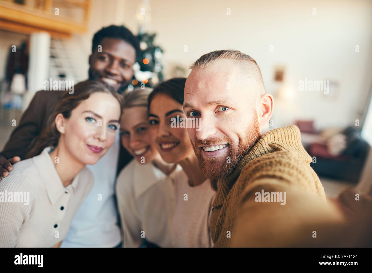 Multi-ethnischen Gruppe der zeitgenössischen erwachsenen Menschen in die Kamera lächeln, während der Einnahme von selfie Foto während der Weihnachtsfeier Stockfoto