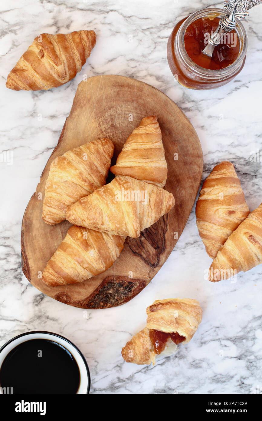 Frische, hausgemachte Croissants oder Halbmond Brötchen mit Marmelade und einer Tasse Kaffee über Marmor Hintergrundbild Schuß von der Ansicht von oben. Stockfoto