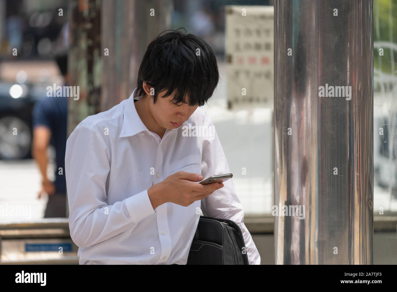 Nahaufnahme von einem Japaner sitzen und entspannen auf einer Bushaltestelle mit einem Telefon in der Hand in Shibuya in Tokio, Japan. Stockfoto
