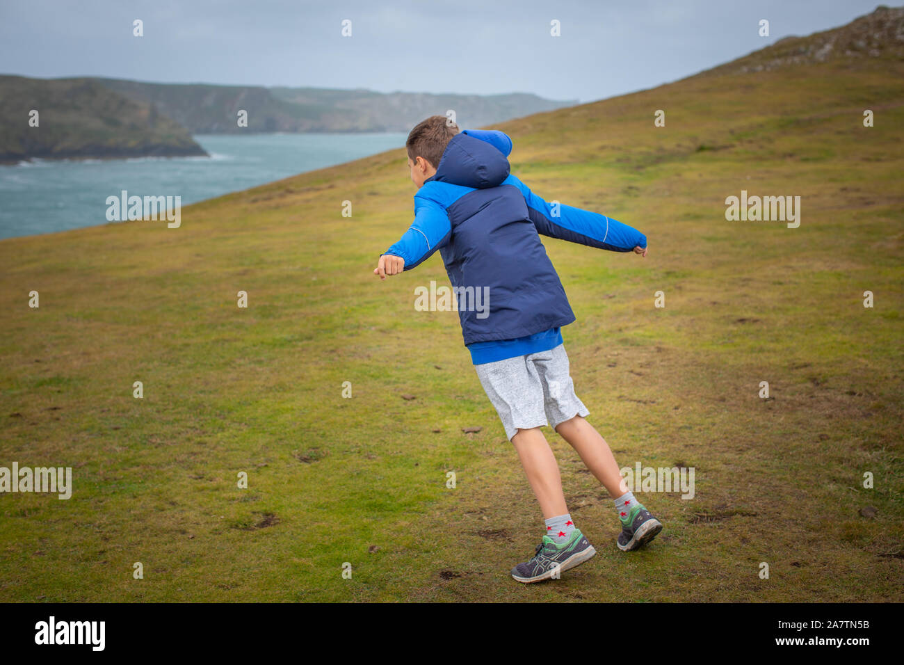 Ein 11 Jahre alter Junge lehnt sich an den starken Winden aus dem Meer, Deer Park, Wales. Stockfoto