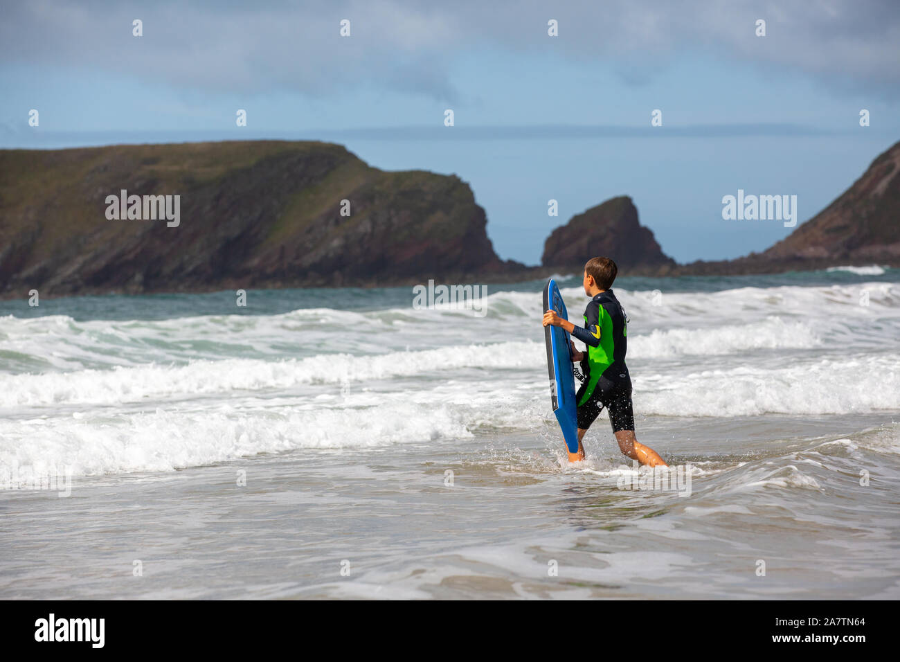 Ein Junge mit seinem Surfbrett in den Wellen, Pembrokeshire, Wales. Stockfoto
