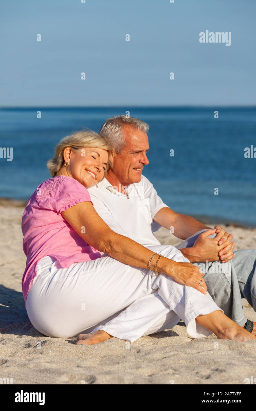 Gerne älterer Mann und Frau Paar sitzen zusammen auf einer einsamen tropischen Strand mit hellen blauen Himmel Stockfoto