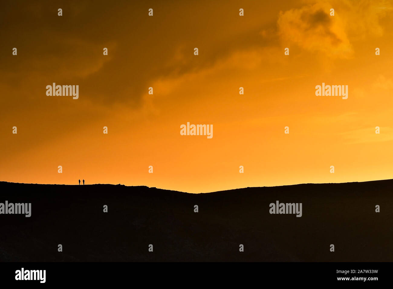 Die winzigen Figuren von zwei Wanderer Silhouette gegen einen intensiven Sonnenuntergang in Newquay in Cornwall. Stockfoto