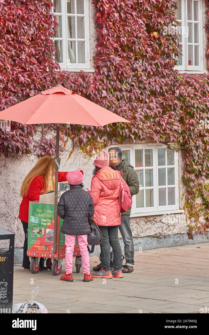 Eine weibliche Verkäufer steht im Herbst auf dem Bürgersteig außerhalb der Efeubewachsene Mauer des Trinity College zu einem Mobile Kiosk und verkauft Eintrittskarten für eine Familie für Stockfoto