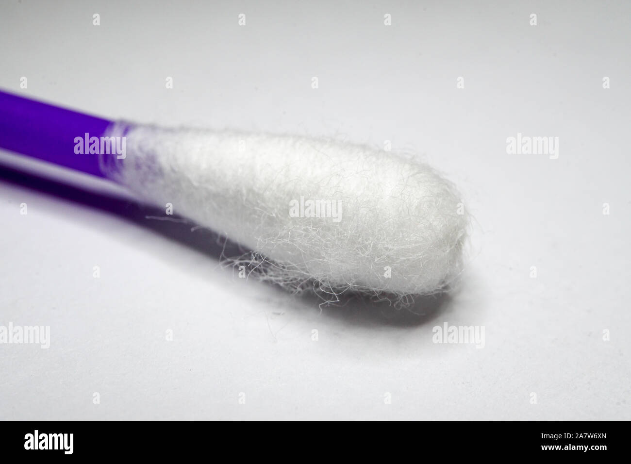 Nahaufnahme der persönlichen Hygiene Werkzeug aus weißer Baumwolle ohr Tupfer q-Tip mit lila Stick und Schatten in teilweise Fokus auf weißem Hintergrund Stockfoto