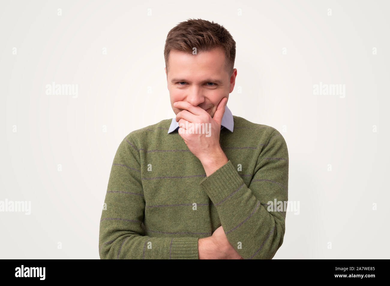 Schüchtern kaukasischen Mann kichert über den Mund mit der Hand. Studio shot Stockfoto