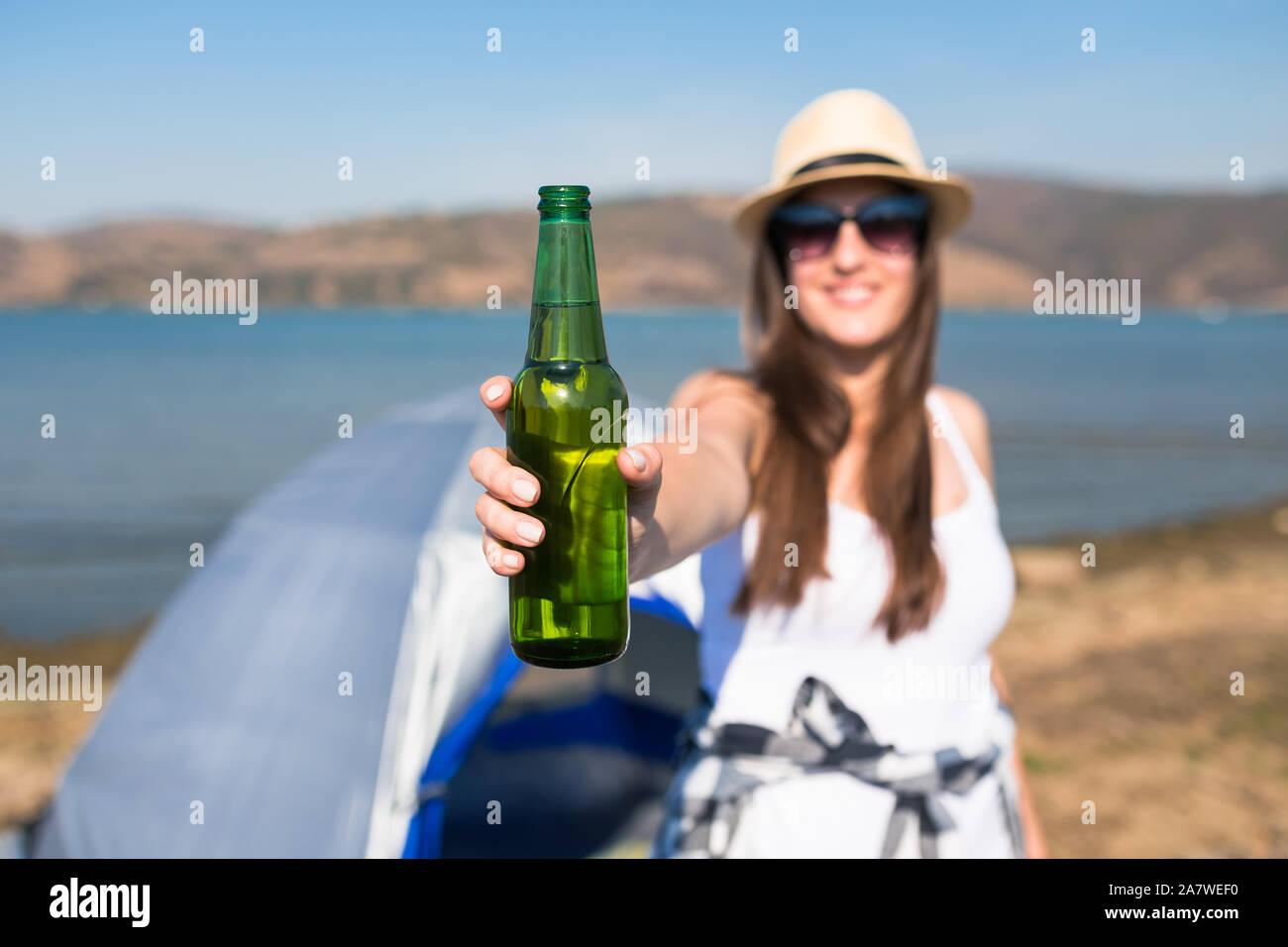 Junge Frau mit Bier Flasche vor Camping Zelt an der Küste. Freiheit und Natur Konzept. Stockfoto