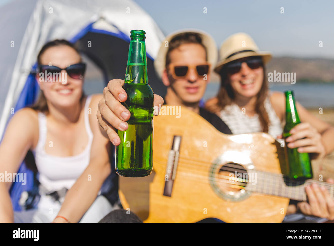 Gitarre Spieler mit Flasche Bier, während eine große Zeit mit seinen Freunden beim Camping am Strand. Stockfoto