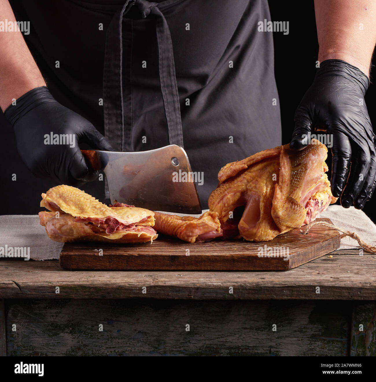 Koch in schwarzen Uniform und Latex Handschuhe Zerkleinern von rohem Huhn  in Stücke auf einem braunen Holzbrett, dunklen Hintergrund, kochen Prozess  Stockfotografie - Alamy