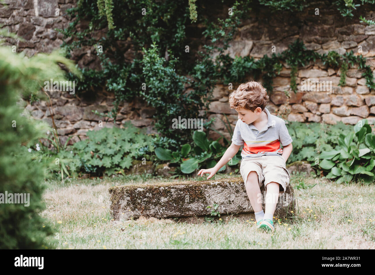 Vorderansicht des Junge sitzt auf bemoosten Felsen - Sitzbank Stockfoto