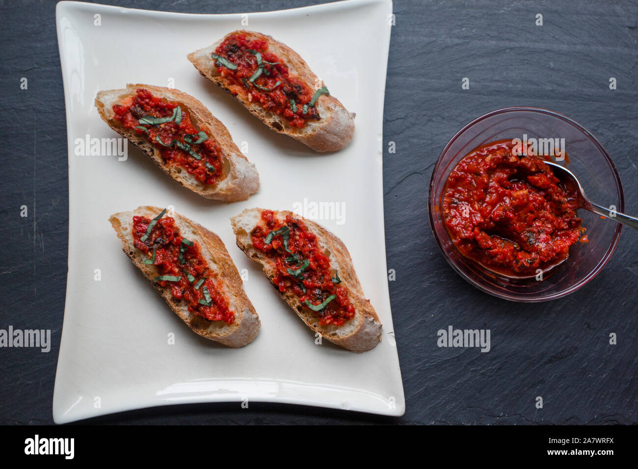 Tomaten - Paprika Bruschetta mit frischem Basilikum auf einem schwarzen Schiefer board Stockfoto